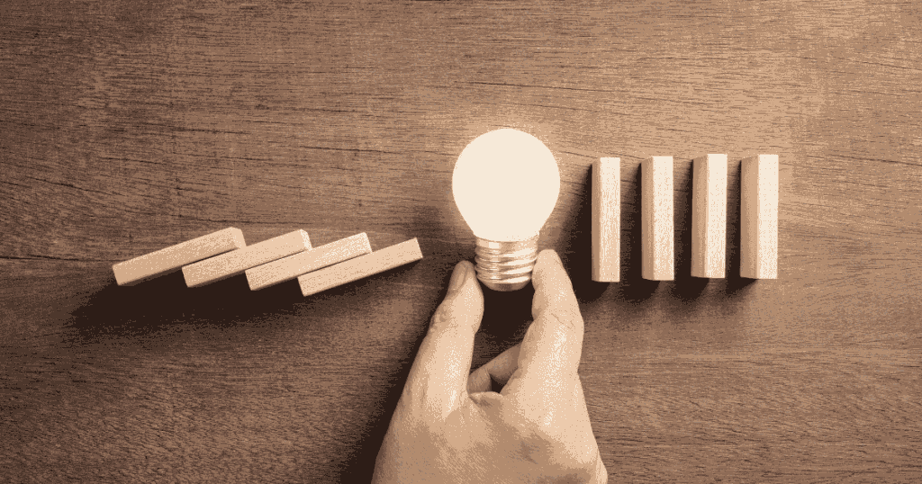 倒れかけたドミノの途中に電球を置いてトラブルを防ぐイメージ