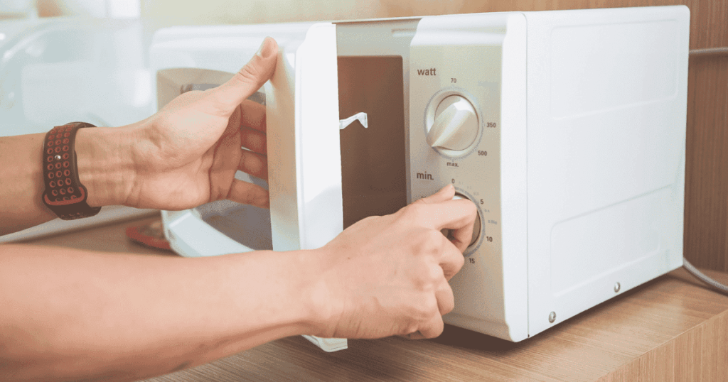 白い単機能電子レンジのタイマーと出力ダイヤルを操作する手元