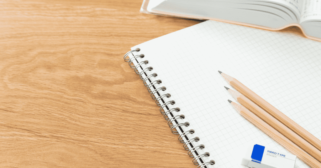方眼ノートと鉛筆3本を置いた木製デスク