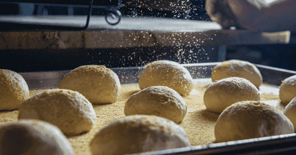 天板に並べたパン生地へ粉を振っている様子