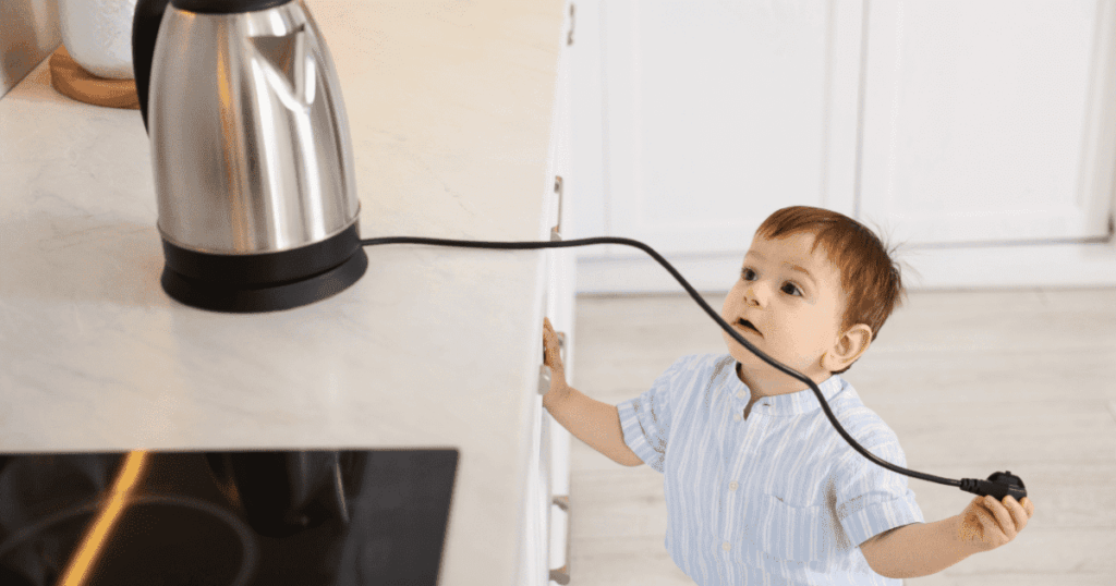 電気ケトルのコードに手を伸ばす小さな子どもの様子
