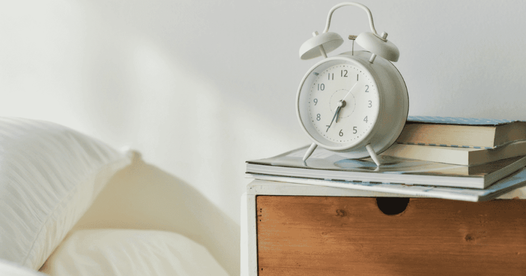 ベッド横の棚に置かれた目覚まし時計と本
