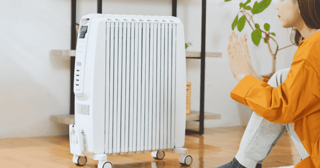 オイルヒーターの前で手を温める女性