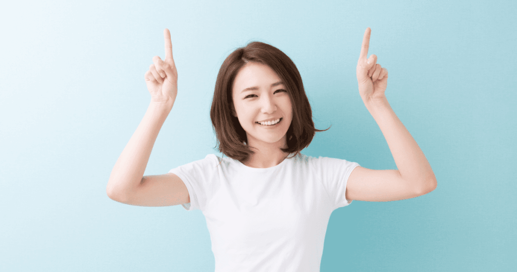 両手の人差し指を上に向けて笑う女性