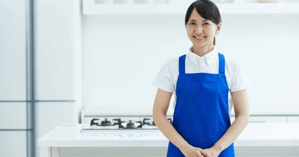 冷蔵庫のあるキッチンに立つ青いエプロン姿の女性
