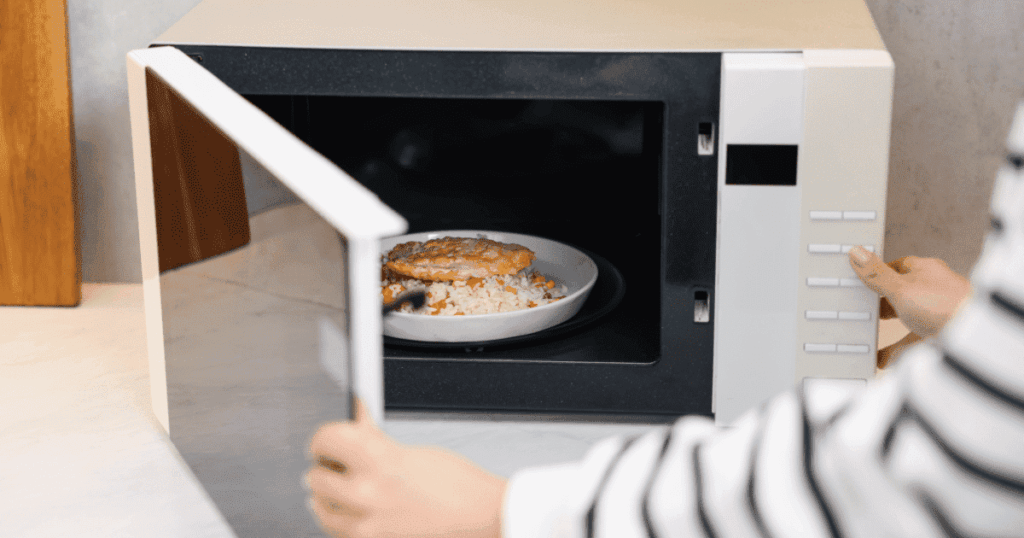 電子レンジの扉を開ける人と庫内に置かれた料理